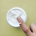 Cream for face or body in white container and female hand on bla